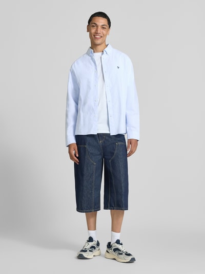 Męski model nosi koszulę casualową z bawełny Freizeithemd aus reiner Baumwolle od REVIEW, prosty krój, Kołnierzyk typu button down, wyhaftowane logo, z długim rękawem, mankiety zapinane na 1 guzik; długość tyłu w rozmiarze M: 73 cm, szerokość ramion w rozmiarze M: 44 cm, długość rękawów w rozmiarze M: 67 cm, jasny niebieski, gładka faktura, kolorowe kontrasty, całkowity widok z przodu.