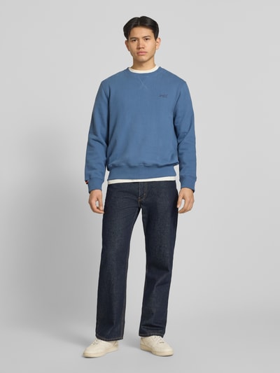 Mannenmodel draagt Sweatshirt met Rundhalsausschnitt und Label-Stitching van Superdry uit katoenmix, regular fit, blauwe kleur, ganzlichaamsaanzicht van voren.
