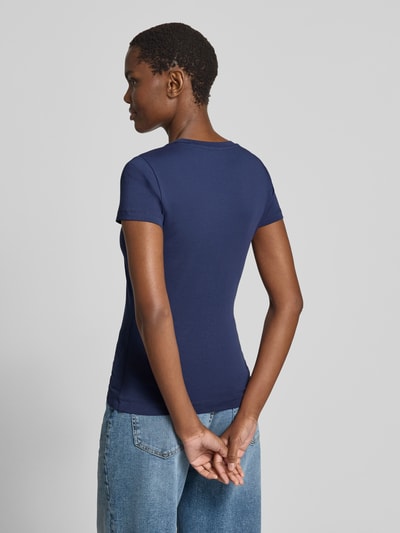 Vrouwenmodel draagt T-shirt met logo en ronde hals van guess, mix van katoen en elastaan, slim fit, ruglengte maat S 58 cm, geheelopname achterkant.