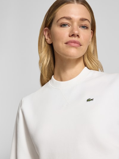 Frauenmodel trägt Relaxed Fit Sweatshirt aus Baumwoll-Mix von Lacoste in Unifarbe Weiß mit Label Patch, Rundhals, Nahaufnahme Oberkörper.