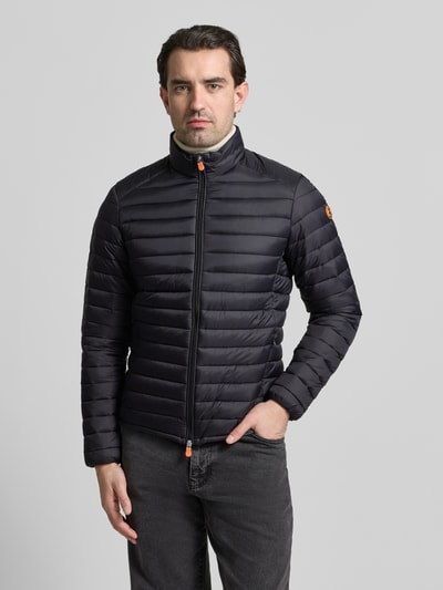 Männermodel trägt schwarze Steppjacke mit Zweiwegereißverschluss Modell 'Alexander' von SAVE THE DUCK, Regular Fit, Ganzkörperansicht von vorne