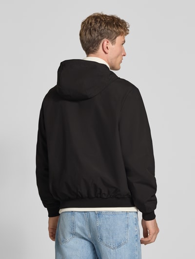 Männermodel trägt Regular Fit Jacke mit Kapuze Modell 'Charge' von JACK & JONES in Schwarz, glatte Struktur, Ganzkörperansicht Rückansicht. Rückenlänge bei Größe M: 68 cm, Schulterbreite: 50 cm, Brustweite: 60 cm, Ärmellänge: 66 cm.