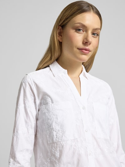 Frauenmodel trägt Regular Fit Hemdbluse mit floralem Allover-Stitching von Christian Berg Woman aus reiner Baumwolle, Weiß mit Hemdblusenkragen, Brusttaschen und durchgängiger Knopfleiste, Nahaufnahme Oberkörper.