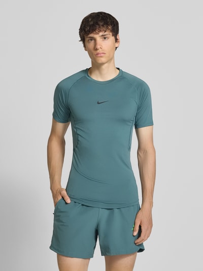 Männermodel trägt T-Shirt mit Logo-Print und Rundhalsausschnitt von NIKE TRAINING, Slim Fit, Raglanärmel, mattgrün, Ganzkörperansicht von vorne.