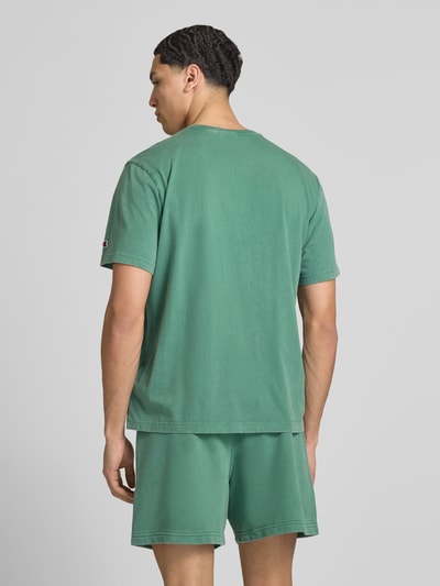 Męski model nosi T-Shirt mit Label-Stitching und Rundhalsausschnitt od CHAMPION, bawełna, krój regular fit, długość tyłu w rozmiarze M 67 cm, zielony, widok całej sylwetki z tyłu.