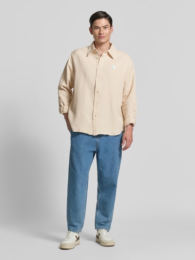 Männermodel trägt beiges Regular Fit Freizeithemd mit Label-Patch von American Vintage aus reiner Baumwolle, Ganzkörperansicht von vorne.