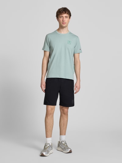 Männermodel trägt Shorts mit Logo und elastischem Bund von CHAMPION aus Baumwoll-Mix in Schwarz, Regular Fit, Ganzkörperansicht von vorne.