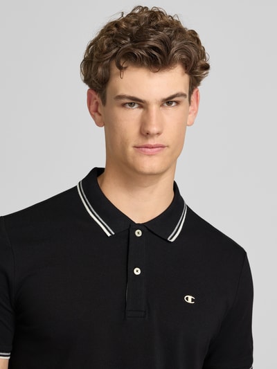 Männermodel trägt Slim Fit Poloshirt mit Label-Stitching von CHAMPION in Schwarz aus Reine Baumwolle, Nahaufnahme Oberkörper.