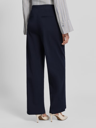 Frauenmodel trägt Stoffhose mit französischen Eingrifftaschen Modell 'Mucia Base' von OPUS PANTS, dunkelblauer Baumwoll-Mix, Loose-Fit, elastischer Bund, Gesäßleistentaschen, Ganzkörperansicht Rückansicht.