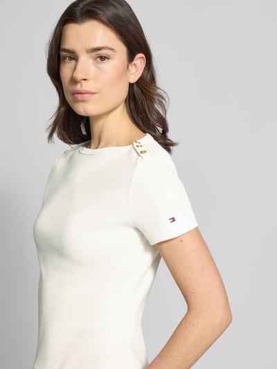 Modelka kobieca nosi Slim Fit T-Shirt aus reiner Baumwolle von Tommy Hilfiger, efekt: jednolity kolor, krój slim fit, detal z logo, ozdobne guziki, dekolt w łódkę, rękaw: krótki, zakończenie rękawów: proste, wykończenie materiału: tkanina, materiał: bawełna. Ujęcie: z przodu, do połowy ciała.