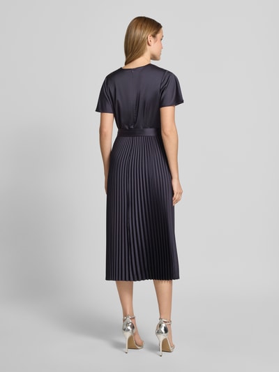 Frauenmodel trägt Midikleid aus Satin mit V-Ausschnitt von Comma, taillierte Passform, Plissee-Optik, kurzärmelig, Stoffband, Ganzkörperansicht Rückansicht.