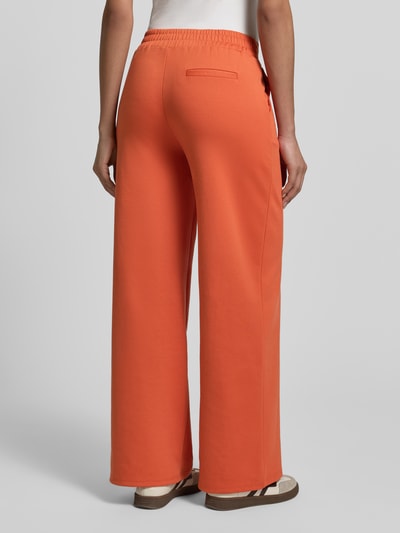 Kobiece modelka nosi spodnie materiałowe Wide Fit Stoffhose mit Viskose-Anteil Modell 'Kate' od ICHI, elastyczna mieszanka materiałów z dodatkiem wiskozy, zakładki w pasie, elastyczny pas, długość wewnętrzna nogawki 79 cm dla rozmiaru S, kolor pomarańczowy, gładka tekstura, pełny widok sylwetki od tyłu.