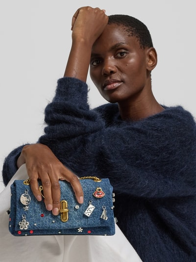 Frauenmodel trägt Shoulder Bag in Denim-Optik von Marc Jacobs mit Überschlag, Ketten-Optik, Zierbesatz, Reißverschlussfach, Ganzkörperansicht von vorne