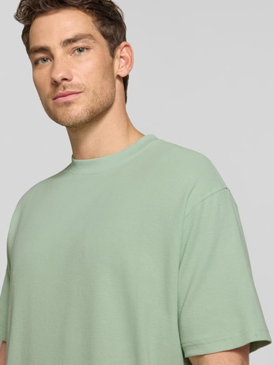 Männermodel trägt Relaxed Fit T-Shirt aus reiner Bio-Baumwolle Modell 'MAARKOS WAFFLE' von Armedangels in Mintgrün, Waffle-Struktur, Logo-Stitching, Rundhals, kurzarm, Feinstrick, Nahaufnahme Oberkörper.