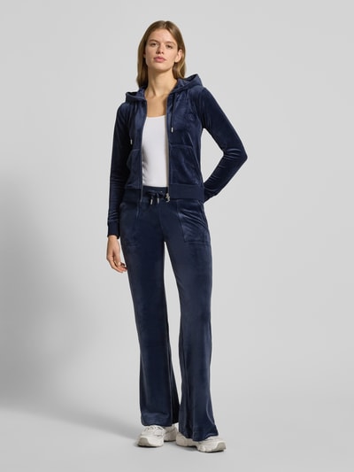 Frauenmodel trägt Sweatjacke mit Label-Stitching Modell 'ROBERTSON' von Juicy Couture aus dunkelblauem Material-Mix mit Stretch-Anteil, Regular Fit, Kapuze mit Tunnelzug, Reißverschluss, Känguru-Tasche; Ganzkörperansicht von vorne.
