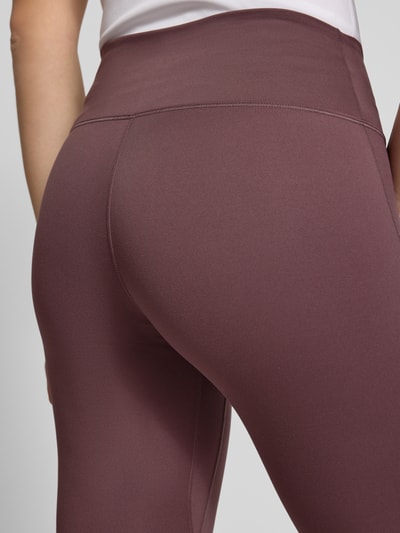 Frauenmodel trägt Leggings mit Logo von NIKE TRAINING in Mauve, glatte Textur, körpernahe Passform, Nahaufnahme Hüftbereich.