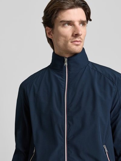 Männermodel trägt Jacke mit Stehkragen von Christian Berg Men in Dunkelblau, glatte Textur, Reißverschlusstaschen, Nahaufnahme Oberkörper.