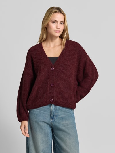 Frauenmodel trägt Oversized Cardigan mit Alpaka-Anteil Modell 'East' von American Vintage in Bordeaux, Strick-Optik, V-Ausschnitt, Ganzkörperansicht von vorne.