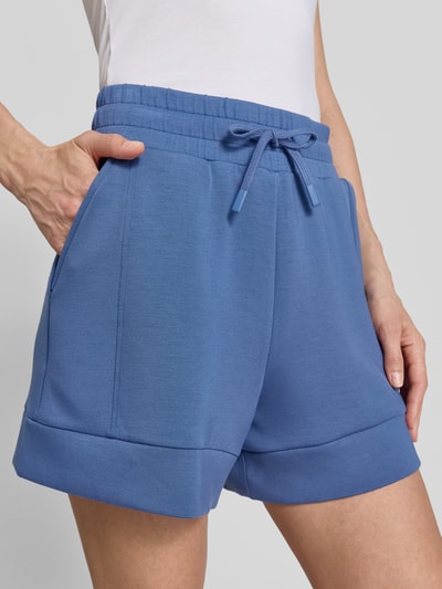 Frauenmodel trägt Shorts mit Eingrifftaschen Modell 'atrium' von VARLEY, blauer Viskose-Mix mit Stretch-Anteil, Elastischer Bund mit Kordelzug, High-Rise-Fit, Nahaufnahme Oberkörper.