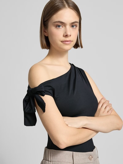 Frauenmodel trägt T-Shirt im One-Shoulder-Look von Gina Tricot aus Material-Mix mit Stretch-Anteil, Knotendetail, Schwarz, Slim-Fit, Nahaufnahme Oberkörper. Rückenlänge bei Größe S: 51 cm.