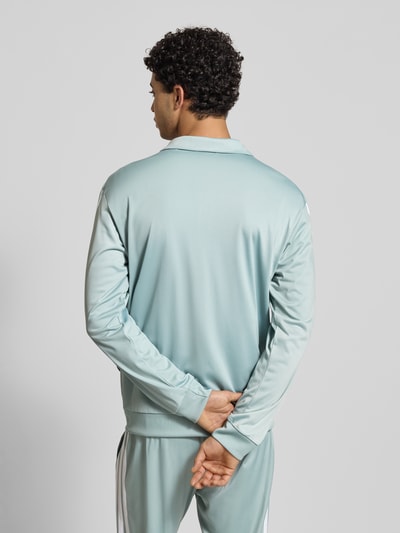 Mannenmodel draagt trainingsjack met logo van adidas Sportswear in lichtblauw, regular fit, opstaande kraag, ruglengte maat M 71 cm, mouwlengte maat M 65 cm, ritssluiting, gladde textuur, ganzebodyaanzicht achteraan