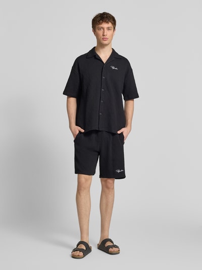 Männermodel trägt czarne szorty z mieszanki bawełny o kroju loose fit, wyhaftowane logo, model 'Jovren' od Pegador, wpuszczane kieszenie, elastyczny pas, szerokość w rozmiarze M: 38 cm, długość wewnętrzna nogawki: 24 cm, Ganzkörperansicht von vorne.