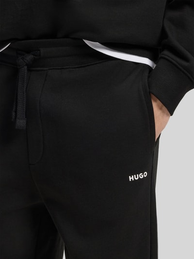Männermodel trägt Regular Fit Jogginghose aus reiner Baumwolle Modell 'DAYOTE232' von HUGO, unifarben schwarz, Label Print, Nahaufnahme Hüfte.