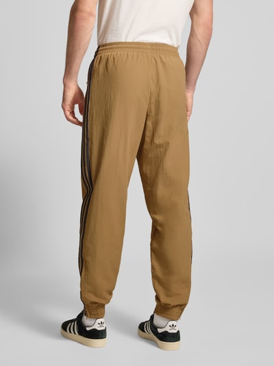 Męski model nosi Sweatpants mit elastischem Bund od adidas Originals, luźny krój, elastyczny pas, beżowy, widok całej sylwetki z tyłu.