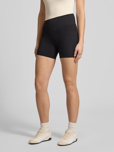 Frauenmodel trägt Slim Fit Shorts mit Logo-Print Modell 'Wander' von P.E Nation aus schwarzem Elastischer-Material-Mix, Ganzkörperansicht von vorne.