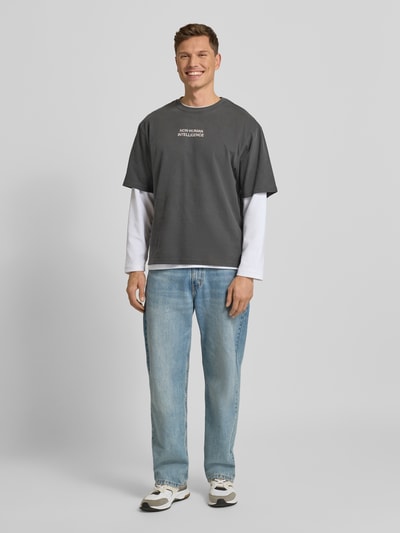 Männermodel trägt T-Shirt mit Rundhalsausschnitt Modell 'Gary' von Wood Wood in Dunkelgrau, Relaxed Fit, reine Baumwolle, Ganzkörperansicht von vorne.