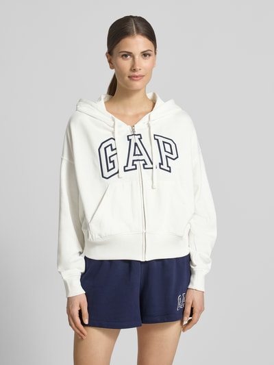 Vrouwenmodel draagt Regular Fit sweatjack met logo-stitching model 'Heritage' van GAP, katoenmix, capuchon met tunnelkoord, kangoeroezak, elastische boorden, voorkant borstlogo, kleur wit, textuur zacht, contrast navy, nahaufnahme bovenlichaam.