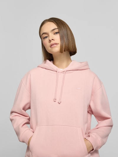 Vrouwenmodel draagt Hoodie met Kapuze van Levi's®, lichtroze, losse pasvorm, kangoeroezak, label-stitching. Nahaufnahme bovenlichaam.