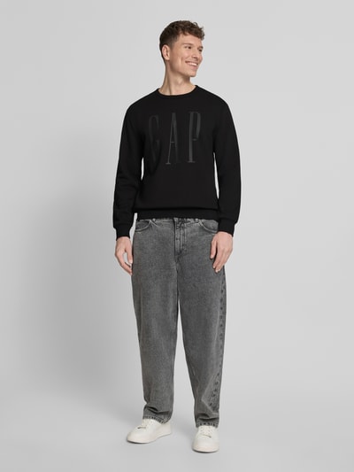 Männermodel trägt schwarzes Sweatshirt mit Rundhalsausschnitt und Logo von GAP, Baumwoll-Mix, Regular-Fit, Ganzkörperansicht von vorne.