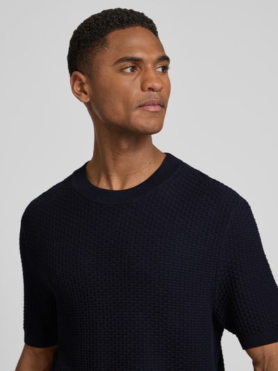 Mężczyzna nosi Regular Fit Strick-Shirt aus reiner Baumwolle Modell 'H-NILTON' od BOSS, kolor granatowy, faktura strukturalna, okrągły dekolt, krótkie rękawy, dzianina, widok na górną część sylwetki z przodu.