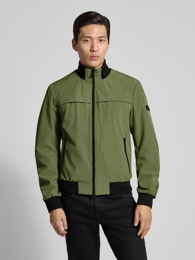 Mężczyzna model nosi kurtkę Peuterey Jacke mit Stehkragen Modell 'POTOSI' z mieszanki materiałów z dodatkiem streczu, krój regular fit, zamek błyskawiczny dwustronny, stójka, długość tyłu w rozmiarze M: 64 cm, szerokość ramion w rozmiarze M: 49 cm, szerokość klatki piersiowej w rozmiarze M: 59 cm, długość rękawów w rozmiarze M: 67 cm, kolor zielony z czarnymi detalami, faktura gładka, całkowity widok z przodu.