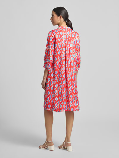 Frauenmodel trägt Knielanges Hemdblusenkleid mit V-Ausschnitt von Milano Italy in Rot mit Allover-Muster, lockere A-Linie, Rückenansicht.
