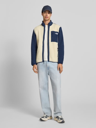 Männermodel trägt Fleecejacke mit Label-Stitching Modell 'Yumiori' von The North Face in Beige und Dunkelblau, Regular-Fit, Stehkragen, Reißverschluss, Reißverschlusstaschen; Rückenlänge bei Größe M 67 cm, Ärmellänge 70 cm. Ganzkörperansicht von vorne.