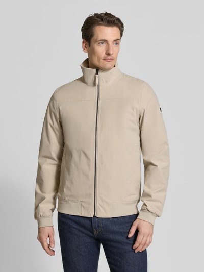 Männermodel trägt Regular Fit Jacke mit Stehkragen Modell 'Alvin' von Didriksons in Beige, glatte Textur, Eingrifftaschen, Ganzkörperansicht von vorne
