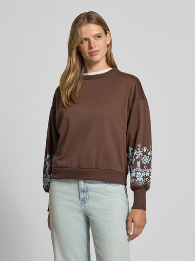 Frauenmodel trägt Relaxed Fit Sweatshirt aus reiner Baumwoll-Mix Modell 'BROOKE' von ONLY, braun mit weißen Blumenmustern, Damen Sweatshirt von ONLY, Ganzkörperansicht von vorne.