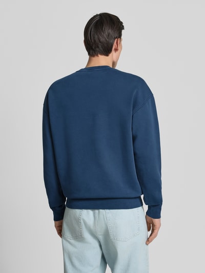 Männermodel trägt Relaxed Fit Sweatshirt aus reiner Bio-Baumwolle Modell 'ICONIC GMT DYE' von Armedangels, unifarbenes Dunkelblau, Sweat-Material, Ganzkörperansicht Rückansicht.