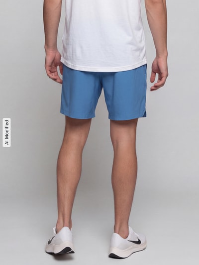 Männermodel trägt Regular Fit Sportshorts mit Logo-Print von Under Armour in Blau, glatte Textur, Ganzkörperansicht Rückansicht, KI-modifiziertes Bild.