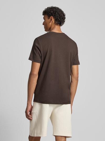 Männermodel trägt T-Shirt mit Logo-Stitching Modell 'Priamo' von JOOP! Collection in Braun, Baumwolle, gerade Form, Ganzkörperansicht Rückansicht.