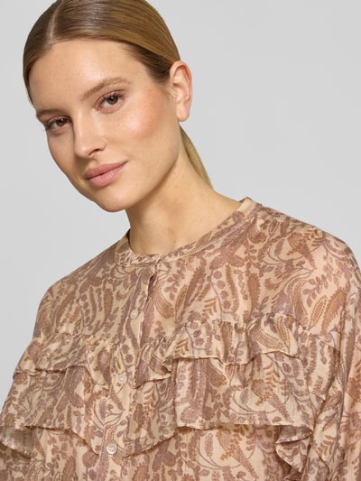 Modelka kobieca ma na sobie bluzkę Regular Fit Bluse mit Volants Modell 'TUNELLA' od Bash, mieszanka lyocellu, okrągły dekolt, falbany, długość tyłu 58 cm, długość rękawów 57 cm, jasnobeżowy i różowy print, faktura półtransparentna. Zbliżenie na górną część ciała z przodu.