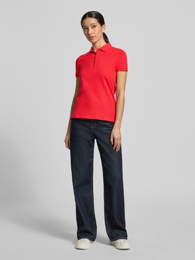 Frauenmodel trägt Slim Fit Poloshirt mit Knopfleiste von Christian Berg Woman, Baumwoll-Elasthan-Mix, leuchtendes Rot, Seitenschlitze, Ganzkörperansicht von vorne. Rückenlänge bei Größe S: 62 cm.