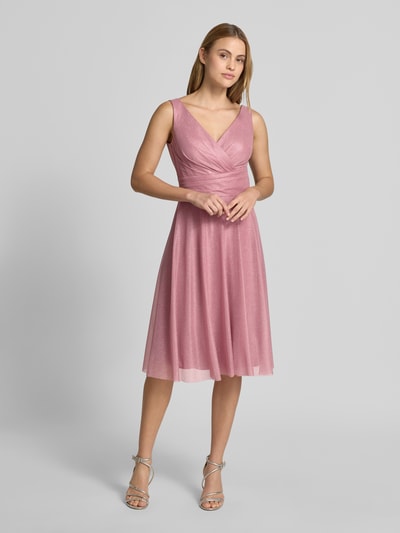 Frauenmodel trägt Knielanges Cocktailkleid mit V-Ausschnitt von TROYDEN COLLECTION in rosa Chiffon, taillierter Schnitt, breite Träger, Rückenausschnitt, Reißverschluss, ganzkörperansicht von vorne. Rückenlänge bei Größe 36: 85 cm, Brustweite 43 cm.