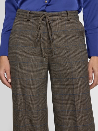 Frauenmodel trägt Stoffhose mit Bügelfalte und Kordelzug von MORE & MORE, braunes Karomuster, French Pockets, Nahaufnahme Oberkörper.