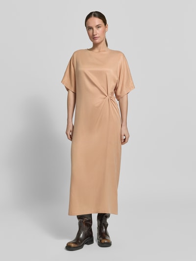 Frauenmodel trägt Midikleid mit Knotendetail Modell 'INDAH' von Drykorn aus Cupro-Baumwoll-Mix, Gerader-Schnitt, Rundhalsausschnitt, Seitenschlitz, beige Ton, glatte Textur, Ganzkörperansicht von vorne.