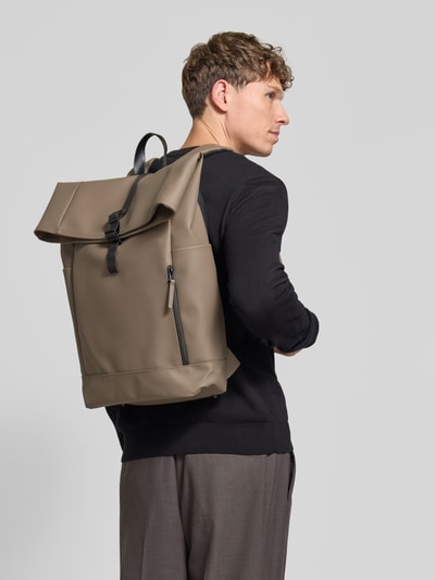 Männermodel trägt Rucksack mit Rolltop Modell 'Splash' von GASTON LUGA in Taupe, matte glatte Textur, große Fronttasche, Ganzkörperansicht Rückansicht. Hauptfach mit Hakenverschluss, verstellbare Schulterriemen, kurzer Henkel, Steck- und Reißverschlussfächer, Maße 42x61x12 cm, Schulterriemen 83 cm.