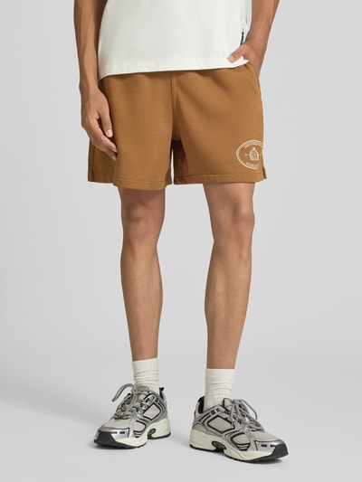 Männermodel trägt Regular Fit Sweatshorts aus Baumwoll-Mix von Nike in Mittelbraun mit weißem Logo, Ganzkörperansicht von vorne. Herren Sweatshorts von Nike