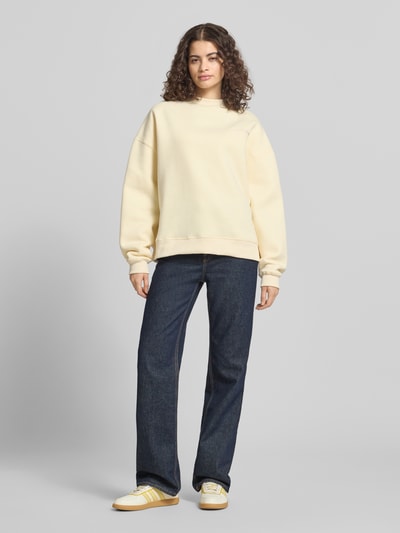 Frauenmodel trägt Relaxed Fit Sweatshirt mit Stehkragen von ANOTHER COTTON LAB, cremefarben, Baumwoll-Mix, elastische Abschlüsse, Ganzkörperansicht von vorne.